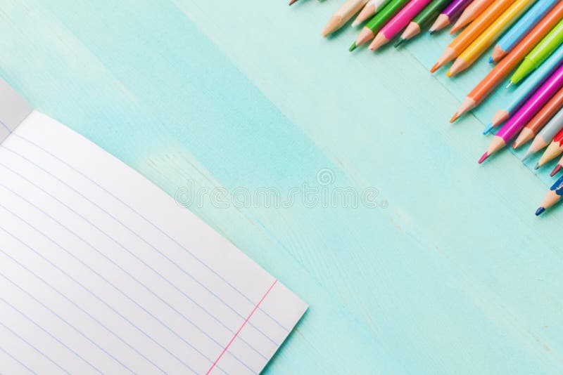 Concept back to school.School accessories, colored pencils, pen with empty notebook on blue wooden background