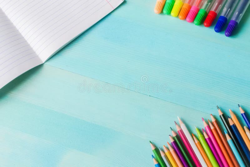 Concept back to school.School accessories, colored pencils, pen with empty notebook on blue wooden background