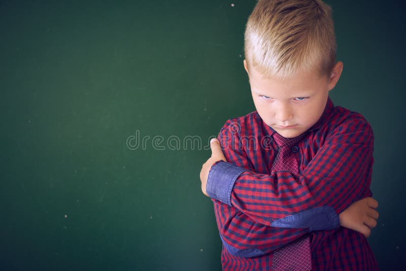 Concept of bullied school boy. Sad and angry little Caucasian boy is hugging himself with his hands standing on the