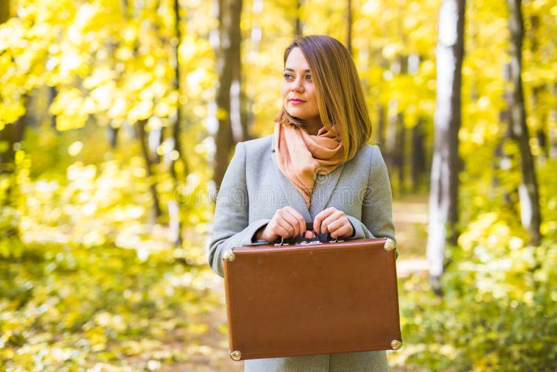 Concept d'automne, de nature et de personnes - portrait de belle femme de sourire avec la valise brune en nature d'automne images libres de droits Concept d'automne, de nature et de personnes - portrait de belle femme de sourire avec la valise brune en nature d'automne images libres de droits