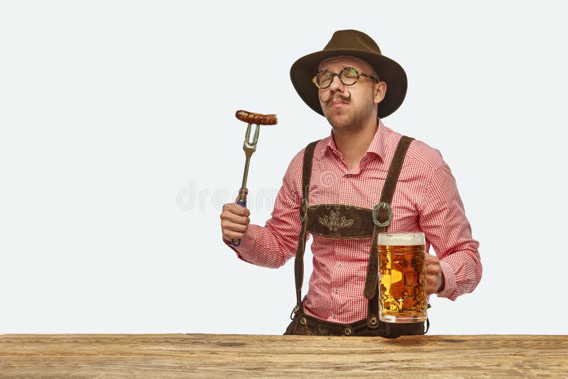 Delightful man wearing traditional fest Bavarian or German outfit with huge beer mug tasting fried sausage. Concept of Oktoberfest, traditions, drinks and food. Copy space for ad. Delightful man wearing traditional fest Bavarian or German outfit with huge beer mug tasting fried sausage. Concept of Oktoberfest, traditions, drinks and food. Copy space for ad