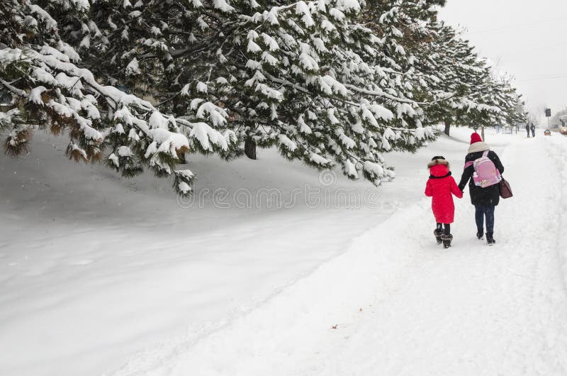 Concept de saison d'hiver Une maman avec sa fille marchent à la maison de l'école avec un sac à dos rose Promenade gentille de fa photos stock Concept de saison d'hiver Une maman avec sa fille marchent à la maison de l'école avec un sac à dos rose Promenade gentille de fa photos stock