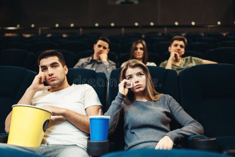 Man and women with popcorn in cinema. Boring film concept, couple watching movie. Man and women with popcorn in cinema. Boring film concept, couple watching movie