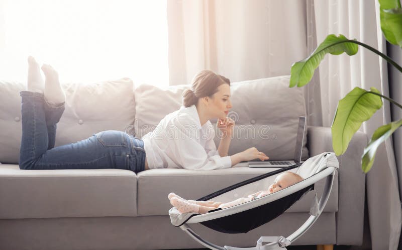 Concept freelance life style maternity leave. Beautiful young mother with baby girl working at home office using laptop