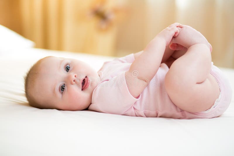 Concept gezond kind Leuke baby die op haar terug op bed in ruimte liggen, die benen met haar handen houden stock fotografie Concept gezond kind Leuke baby die op haar terug op bed in ruimte liggen, die benen met haar handen houden stock fotografie