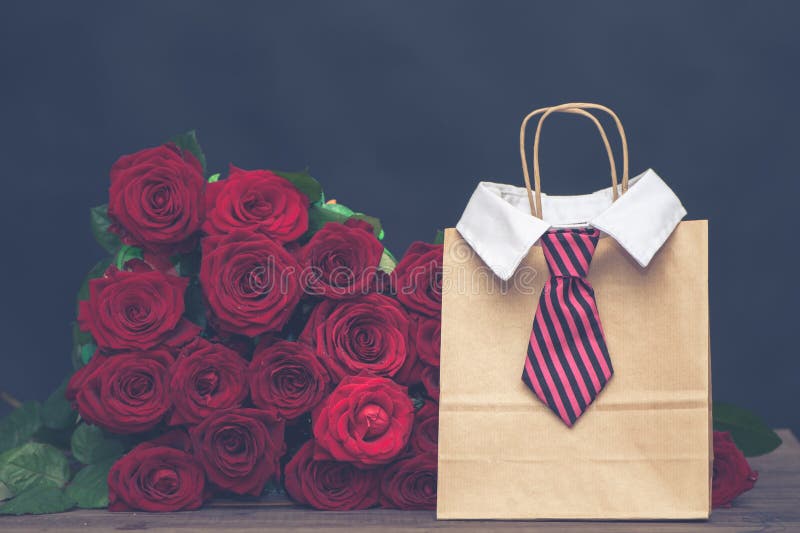 Concept of a gift for the day of lovers from a man.  large armful of red roses and a gift bag with a men`s tie