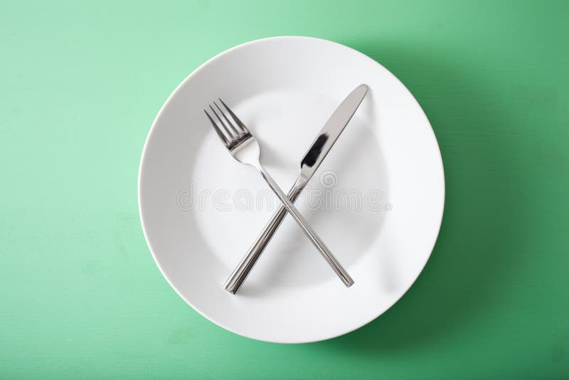 Concept of intermittent fasting and ketogenic diet, weight loss. fork and knife crossed on a plate. Concept of intermittent fasting and ketogenic diet, weight loss. fork and knife crossed on a plate