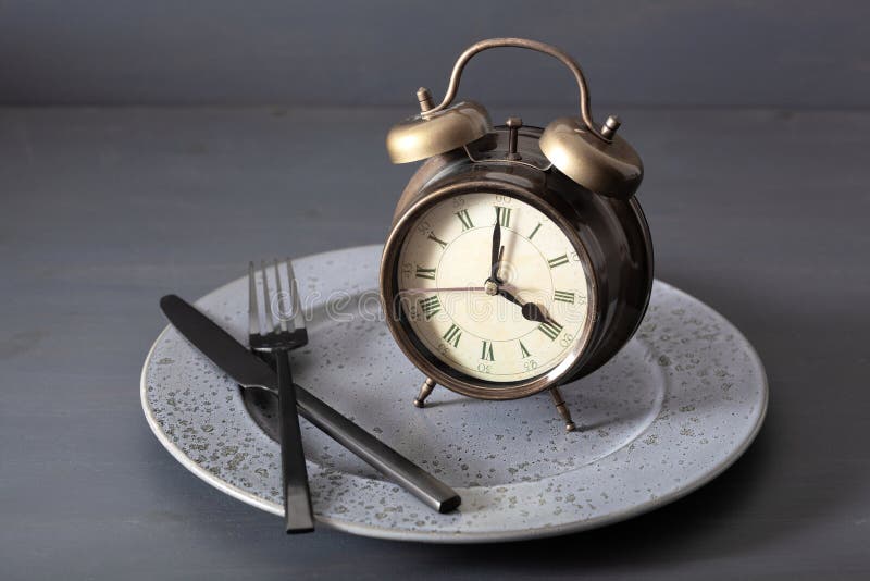 Concept of intermittent fasting, ketogenic diet, weight loss. alarmclock fork and knife on a plate. Concept of intermittent fasting, ketogenic diet, weight loss. alarmclock fork and knife on a plate