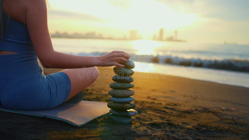 Concept idée équilibre mode de vie sain fitness yoga une femme construit une pyramide de pierres océan coucher de soleil près zen clips vidéos