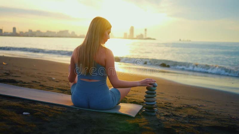 Concept idée équilibre mode de vie sain fitness yoga une femme construit une pyramide de pierres océan coucher de soleil style zen banque de vidéos