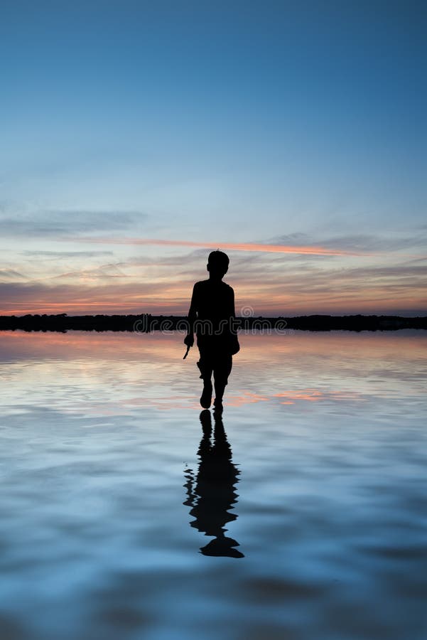 Concept image of young boy walking on water in sunset landscape