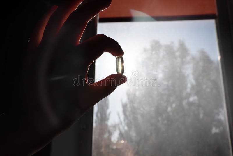 Vitamin D or omega 3 capsules. Vitamin gel in hand against the window. The concept of a lack of vitamin D in the body