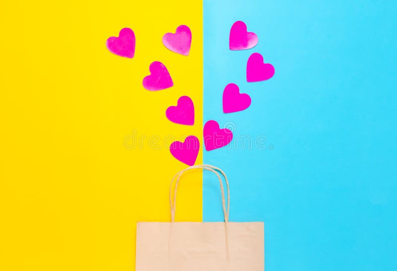 The concept of love of shopping. A paper bag for shopping and lots of decorative hearts on a colored pastel background. Valentine&#x27;s Day. Top view