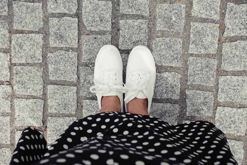 Concept picture of legs walking, Selfie of feet in white sneaker on rock pavement background, top view.