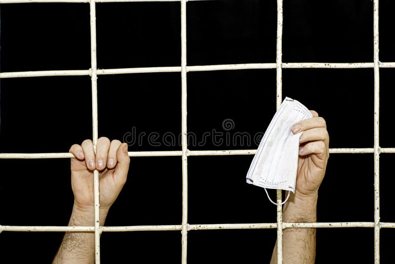 Concept of restriction during the pandemic and quarantine of a person s hand behind an iron bars in his hand medical hygiene mask