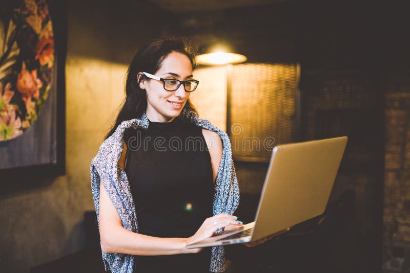 The concept of small business and technology. Young beautiful brunette woman in black dress and gray sweater stands in coffee shop royalty free stock images The concept of small business and technology. Young beautiful brunette woman in black dress and gray sweater stands in coffee shop royalty free stock images