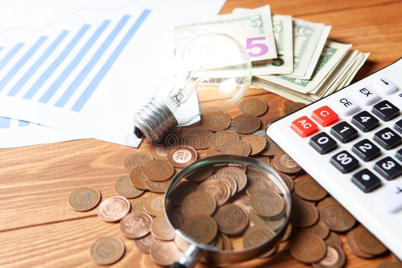 Concept of studying costs. coins next to calculator, magnifier and lamp stock image
