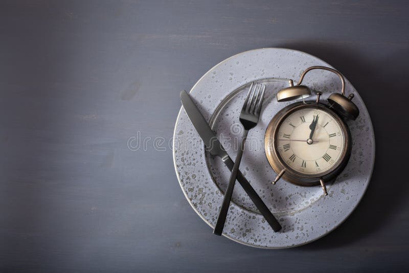 Concept of intermittent fasting, ketogenic diet, weight loss. fork and knife, alarmclock on plate. Concept of intermittent fasting, ketogenic diet, weight loss. fork and knife, alarmclock on plate