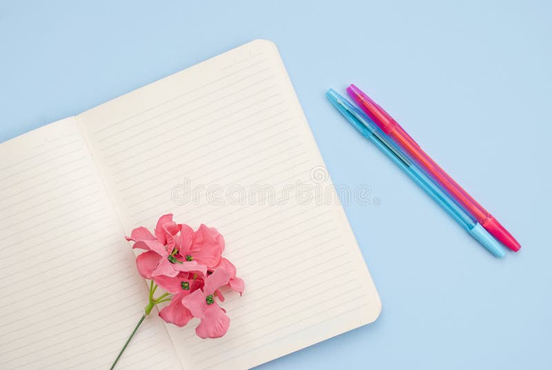 Concept workplace. White open notebook for notes, ballpoint pen, pink flower on a blue background, place for text, copy space. Top