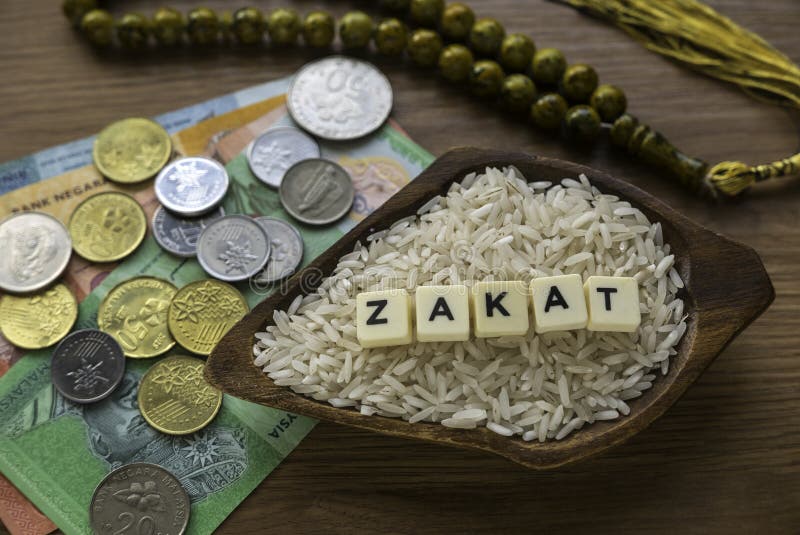 Concept of zakat in Islam religion. Selective focus of money and rice with  alphabet of zakat on wooden background.