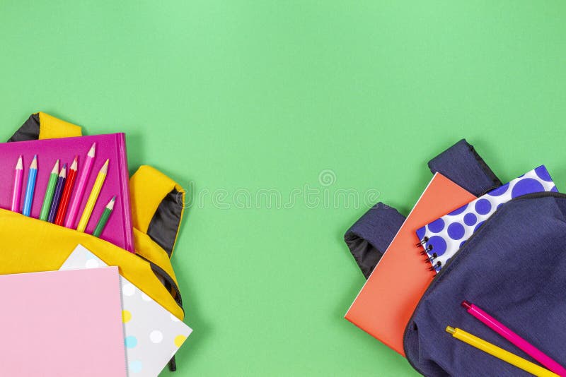 Concept înapoi la școală. rucsacuri galbene și albastre cu cărți și notebook-uri pentru aprovizionarea școlii pe fond verde deschi royalty free stock photography