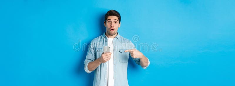 Concepto de aplicaciones y tecnología de compras en línea. hombre impresionado señalando con el dedo al teléfono móvil y mirando foto de archivo