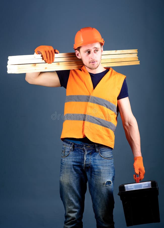 Concepto de la construcción y de la carpintería El carpintero, carpintero, trabajador, constructor en cara soñadora lleva haces d fotografía de archivo Concepto de la construcción y de la carpintería El carpintero, carpintero, trabajador, constructor en cara soñadora lleva haces d fotografía de archivo