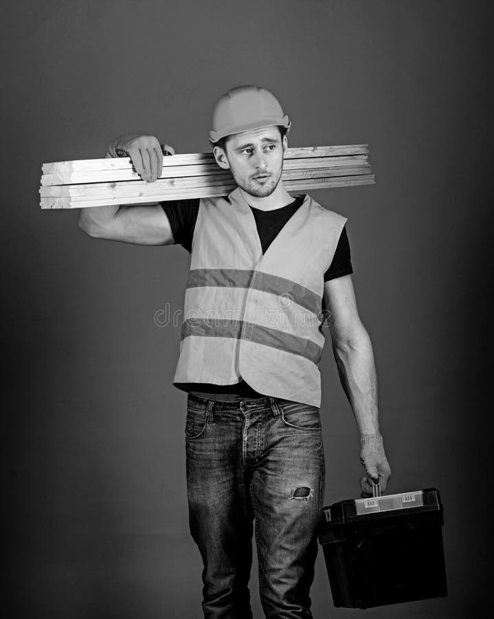 Concepto de la construcción y de la carpintería El hombre en el casco, casco lleva a cabo la caja de herramientas y los haces de fotografía de archivo libre de regalías Concepto de la construcción y de la carpintería El hombre en el casco, casco lleva a cabo la caja de herramientas y los haces de fotografía de archivo libre de regalías