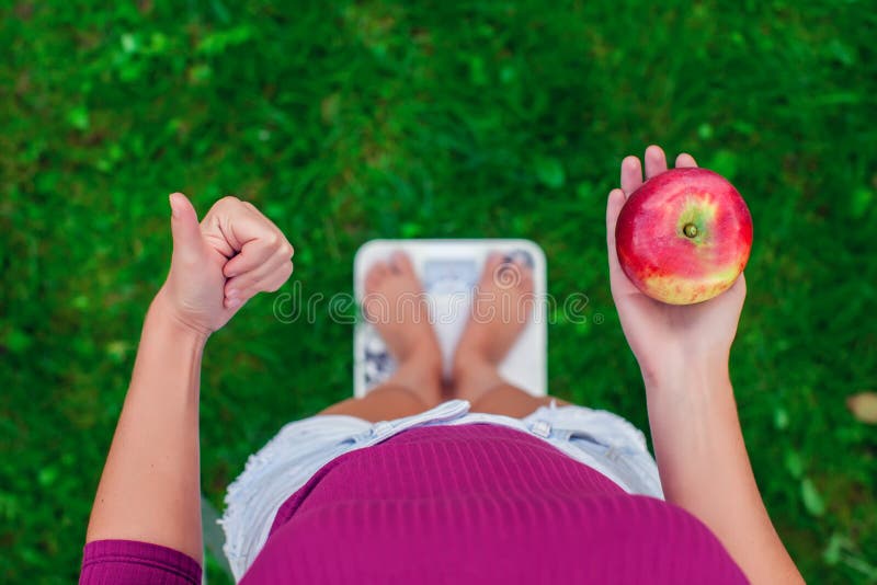 Concepto de la dieta y del peso Mujer joven que se coloca en una escala con imagenes de archivo