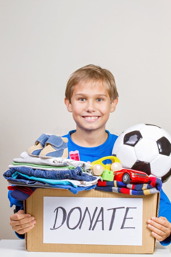 Concepto de la donación El sostenerse del niño dona la caja con ropa, libros y juguetes