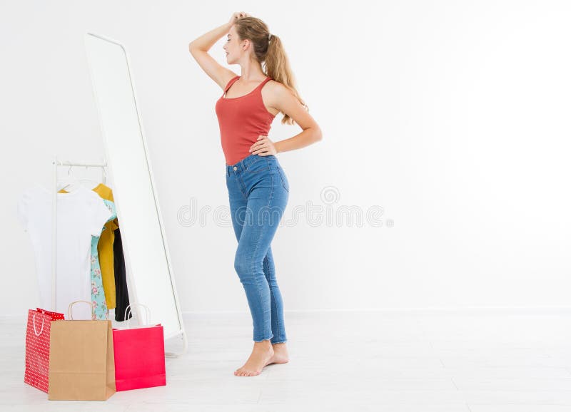 Concepto de la venta de las compras Muchacha rubia en vaqueros y camiseta La mujer joven en la buena forma del cuerpo que mira el