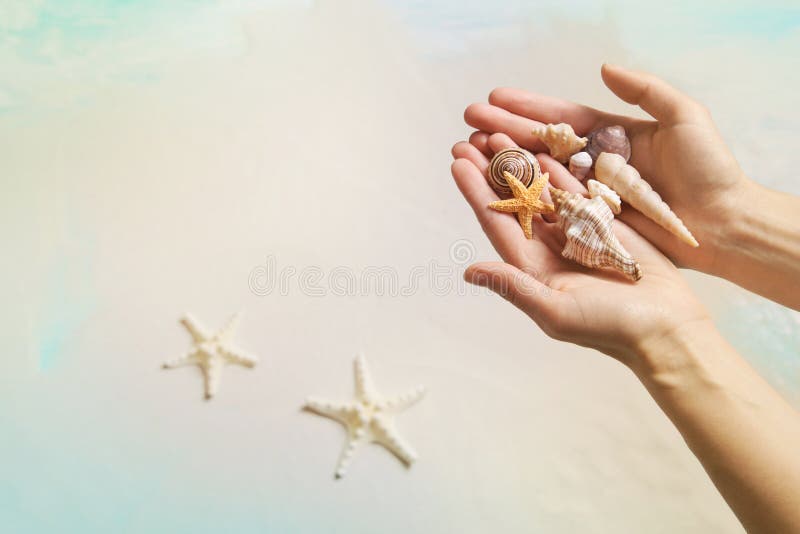 Concepto de las vacaciones de verano: Manos que sostienen cáscaras y estrellas de mar en el th imagenes de archivo Concepto de las vacaciones de verano: Manos que sostienen cáscaras y estrellas de mar en el th imagenes de archivo
