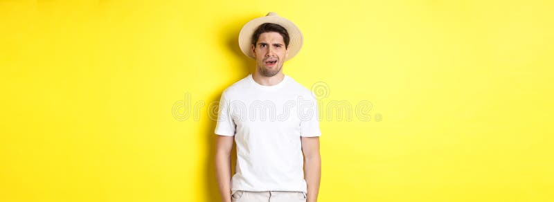 Concepto de turismo y verano. Un tipo confuso que viaja con sombrero de paja y que parece perplejo no puede entender algo de pie foto de archivo