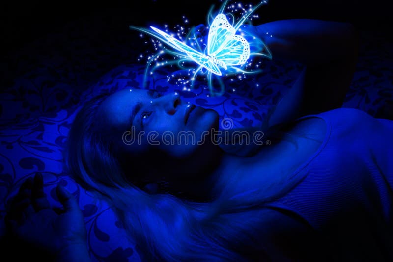 Concepto de una mujer que pone en cama en la oscuridad, iluminado con la luz azul de flotar la mariposa mágica
