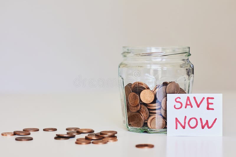 Concepto del dinero del ahorro Tarro de cristal por completo de monedas y de la reserva de la muestra ahora fotografía de archivo Concepto del dinero del ahorro Tarro de cristal por completo de monedas y de la reserva de la muestra ahora fotografía de archivo