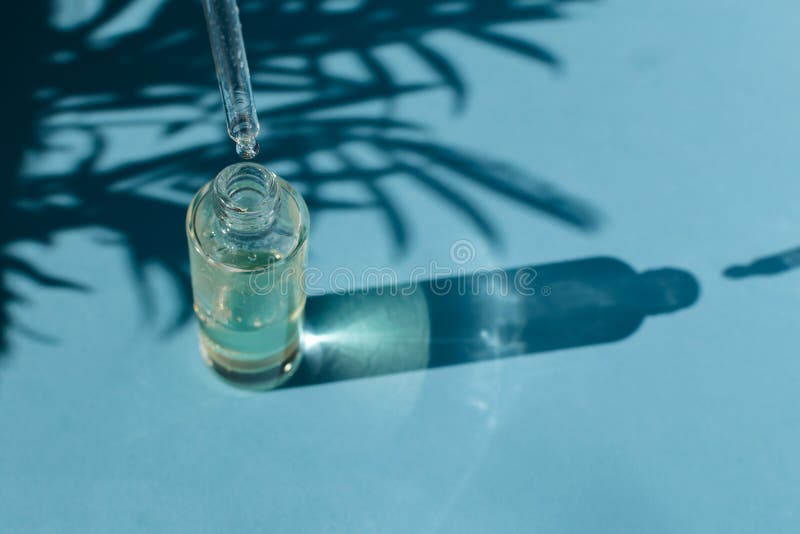 Concepto del skincare de la belleza - el descenso baja de una pipeta en una botella de cristal, fondo azul claro, espacio de la c fotografía de archivo Concepto del skincare de la belleza - el descenso baja de una pipeta en una botella de cristal, fondo azul claro, espacio de la c fotografía de archivo
