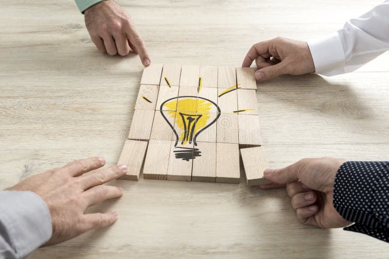 Four businessmen holding pieces of a wooden bricks bearing the image of a light bulb conceptual of business strategy, creativity or teamwork. Four businessmen holding pieces of a wooden bricks bearing the image of a light bulb conceptual of business strategy, creativity or teamwork.