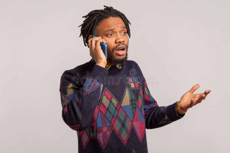 Concerned bearded african guy with dreadlocks talking phone with open mouth and big eyes, shocked disappointed with information