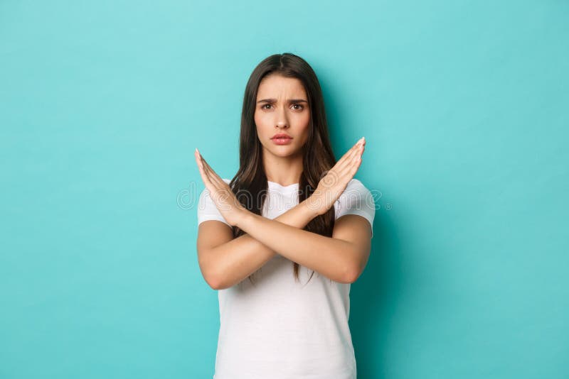 Concerned woman in white t-shirt prohibit something bad, showing cross gesture and frowning displeased, tell to stop