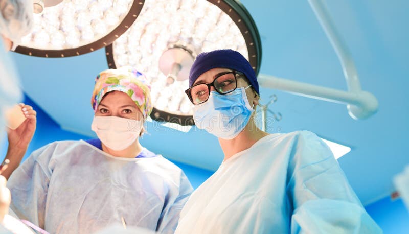 Concetto della chirurgia, della medicina e della gente - tre chirurghi nella sala operatoria all'ospedale durante il loro lavoro immagini stock libere da diritti Concetto della chirurgia, della medicina e della gente - tre chirurghi nella sala operatoria all'ospedale durante il loro lavoro immagini stock libere da diritti