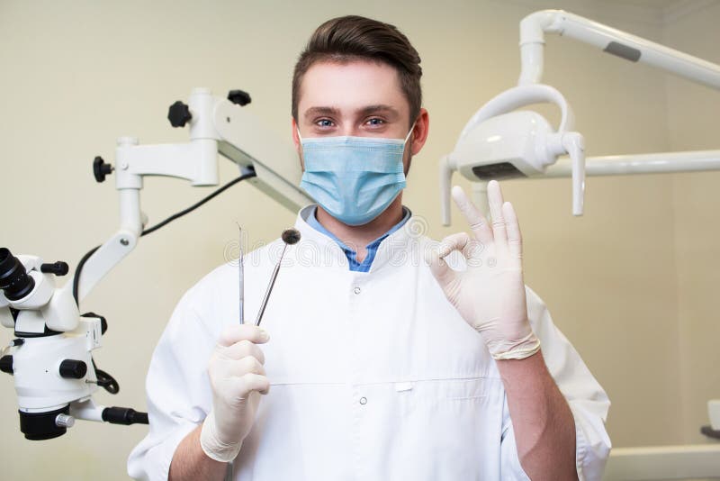 Concetto della gente, della medicina, di stomatologia e di sanità - giovane dentista maschio felice con gli strumenti sopra il fo fotografia stock Concetto della gente, della medicina, di stomatologia e di sanità - giovane dentista maschio felice con gli strumenti sopra il fo fotografia stock