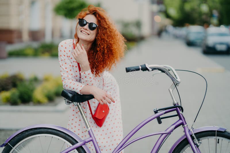 Concetto della gente, di svago, di stile di vita e di ozio La donna riccia allegra messa a fuoco nella distanza, guida la bicicle fotografia stock libera da diritti Concetto della gente, di svago, di stile di vita e di ozio La donna riccia allegra messa a fuoco nella distanza, guida la bicicle fotografia stock libera da diritti
