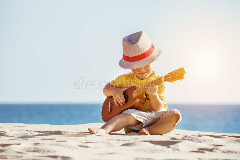 Concetto delle ukulele della chitarra con il ragazzino alla spiaggia immagine stock Concetto delle ukulele della chitarra con il ragazzino alla spiaggia immagine stock