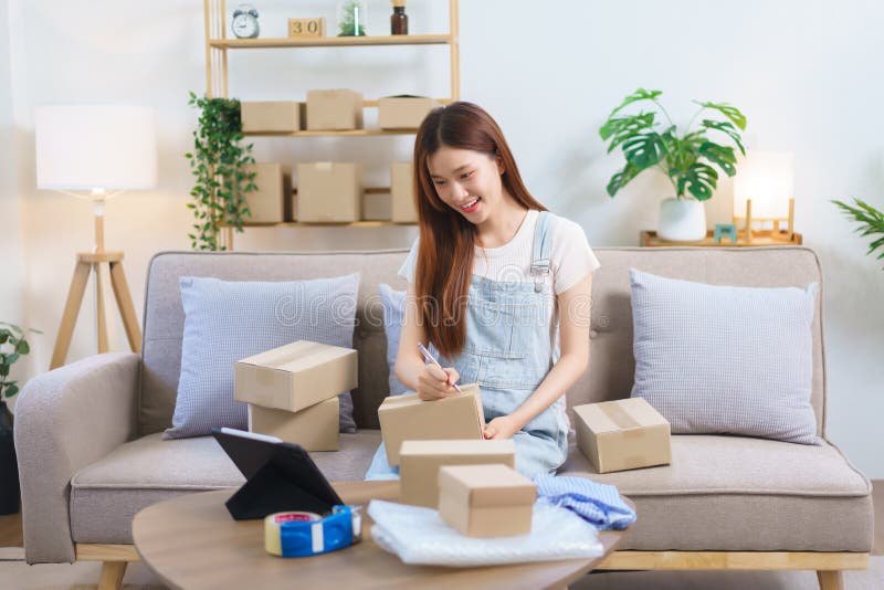 Concetto di commerciante online femmina imprenditrice cerca dati sulla tavoletta e scrive l'indirizzo sulle caselle di pacchi immagine stock