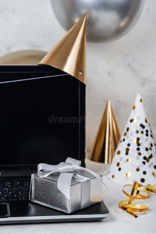 Concetto di festività del compleanno online. scatola argentata per festeggiare sul portatile con cappelli e palloncini da festa immagini stock libere da diritti