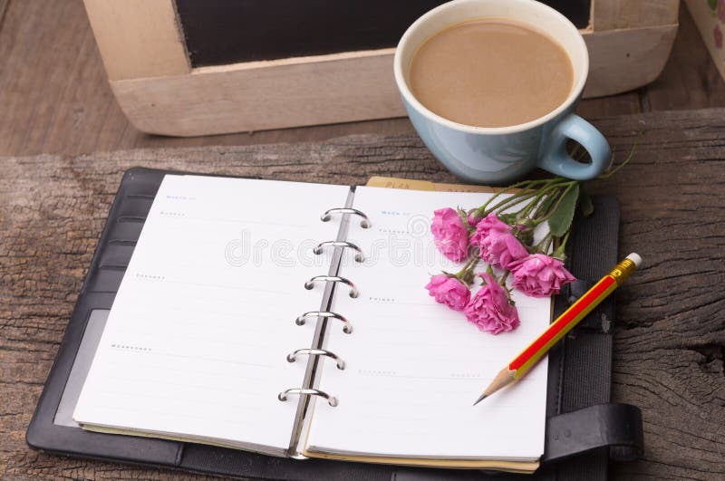 Weekend concept. Pink rose, mug with coffee, diary and pencil on a wooden table. Selective focus, copy space background. Weekend concept. Pink rose, mug with coffee, diary and pencil on a wooden table. Selective focus, copy space background