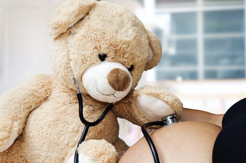 Concetto di gravidanza, della medicina e di sanità - chiuda su dell'orsacchiotto che gioca al dottore lo stetoscopio ed ascolta s fotografia stock Concetto di gravidanza, della medicina e di sanità - chiuda su dell'orsacchiotto che gioca al dottore lo stetoscopio ed ascolta s fotografia stock