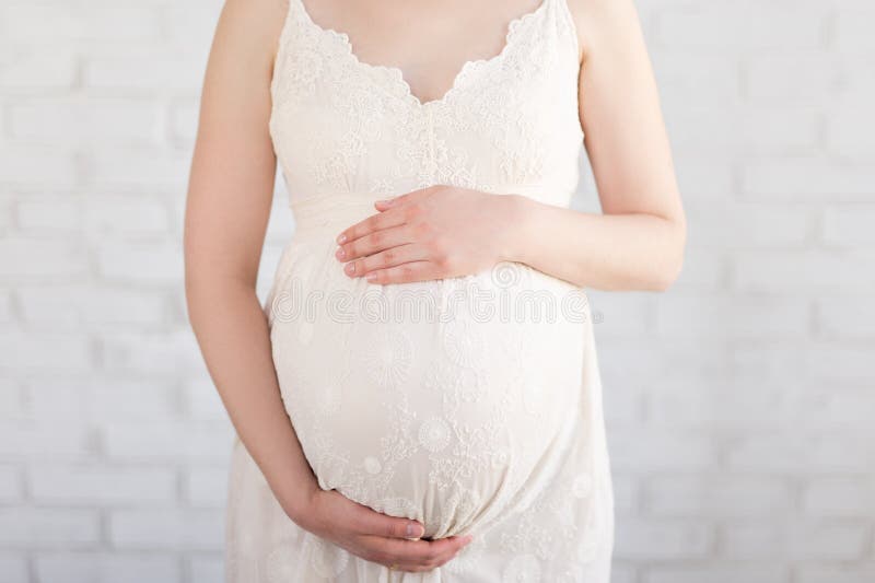 Concetto di gravidanza - vicino su della pancia incinta sopra la parete bianca