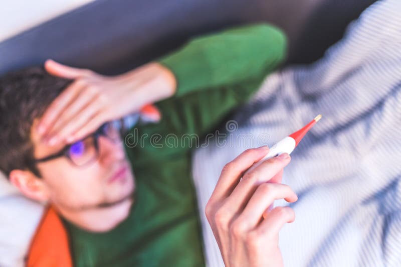 Concetto di influenza e corona : l'uomo tiene in mano un termometro per la febbre da vicino