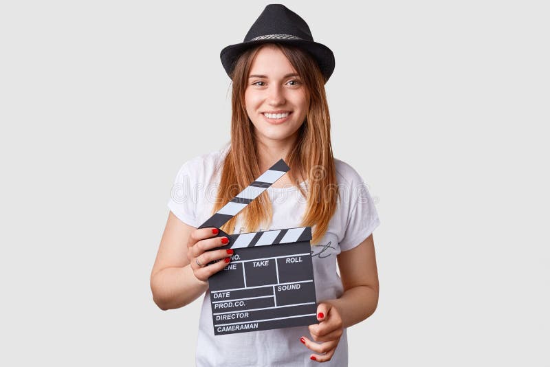 Concetto di produzione cinematografica La femmina caucasica piacevole tiene la valvola di film, porta il cappello alla moda e la immagini stock libere da diritti Concetto di produzione cinematografica La femmina caucasica piacevole tiene la valvola di film, porta il cappello alla moda e la immagini stock libere da diritti